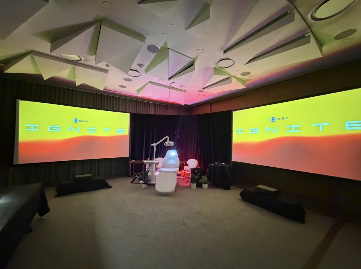 The IGNITE 2026 session room with Stribe IGNITE on both screens and the treatment chair at center